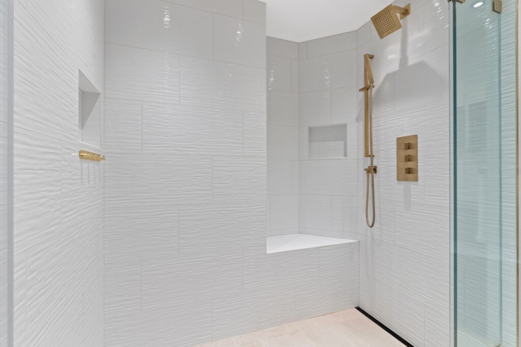 Contemporary white tiled shower with gold fixtures and glass door.