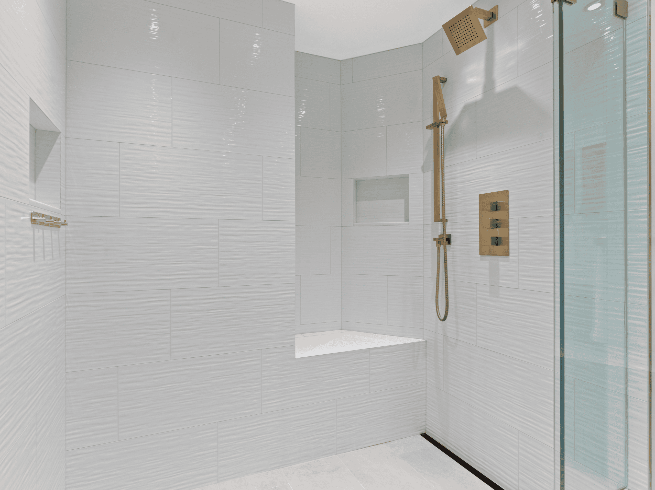 Elegant white tiled shower with gold fixtures and a built-in niche.