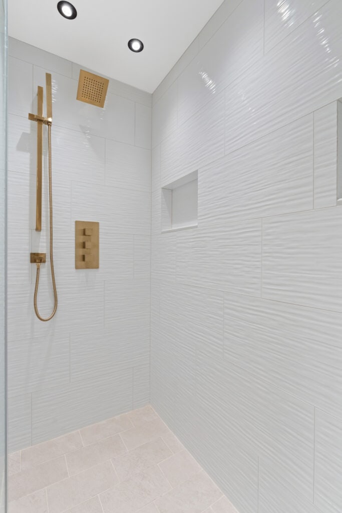Minimalist white shower with gold fixtures and built-in niche.