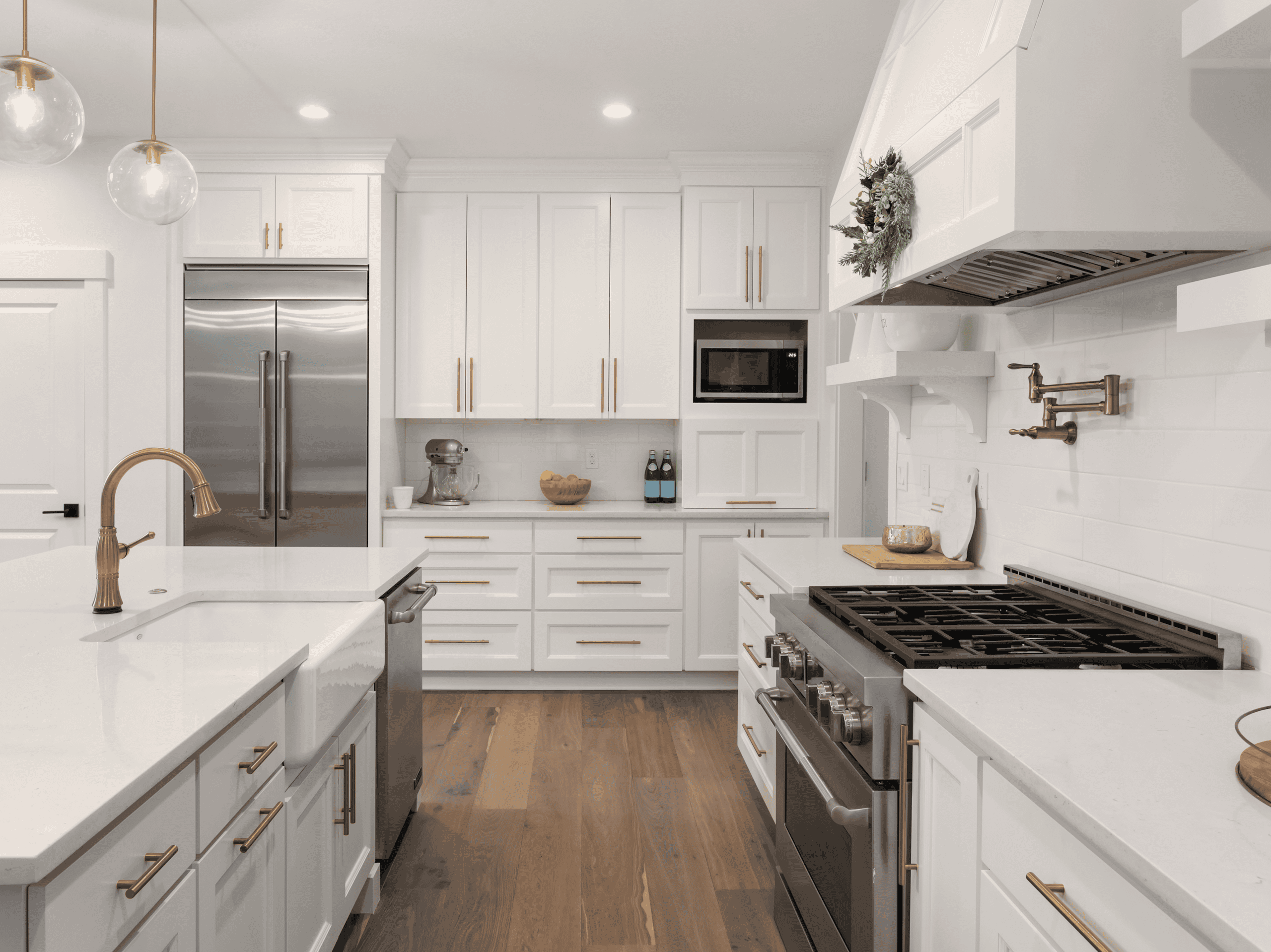 Bright modern white kitchen with gold accents, stainless steel appliances, and wooden flooring.