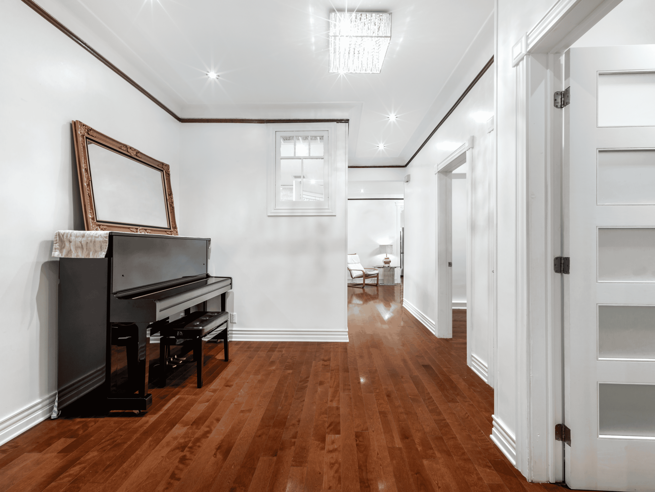 Example Co Interior Elegant living room with hardwood floors, white walls, and a black piano with a mirror above it.