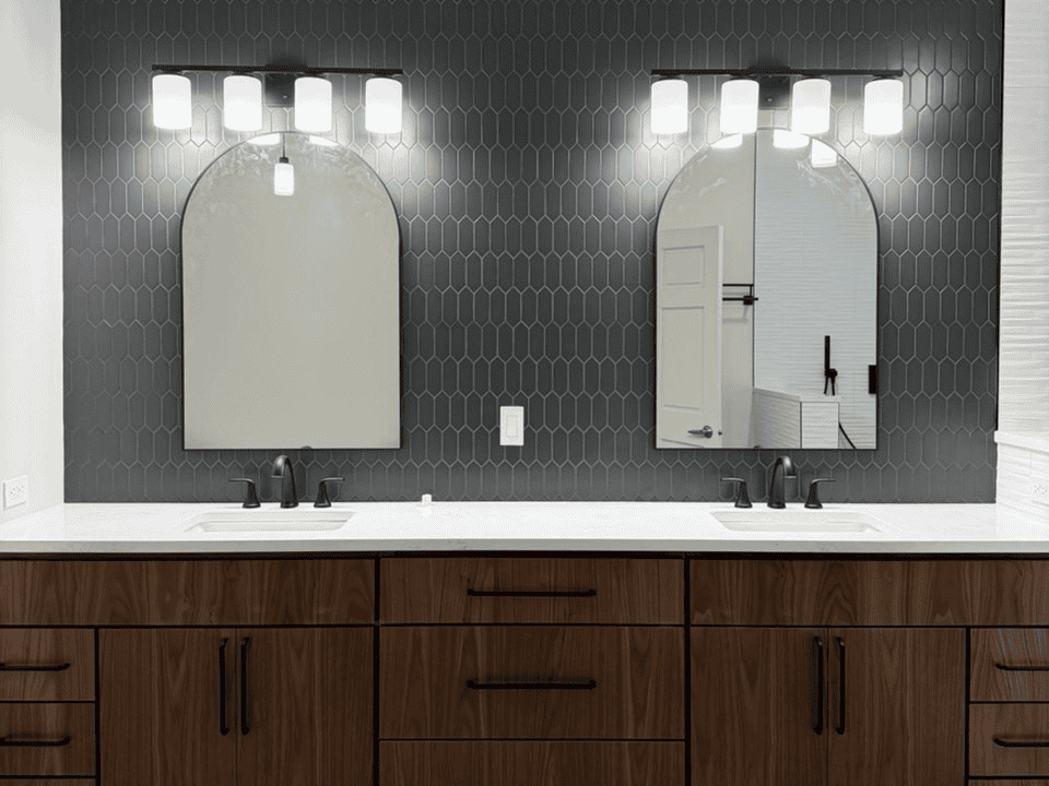 Double bathroom vanity with two mirrors, black hexagon tile wall, and wooden cabinetry.