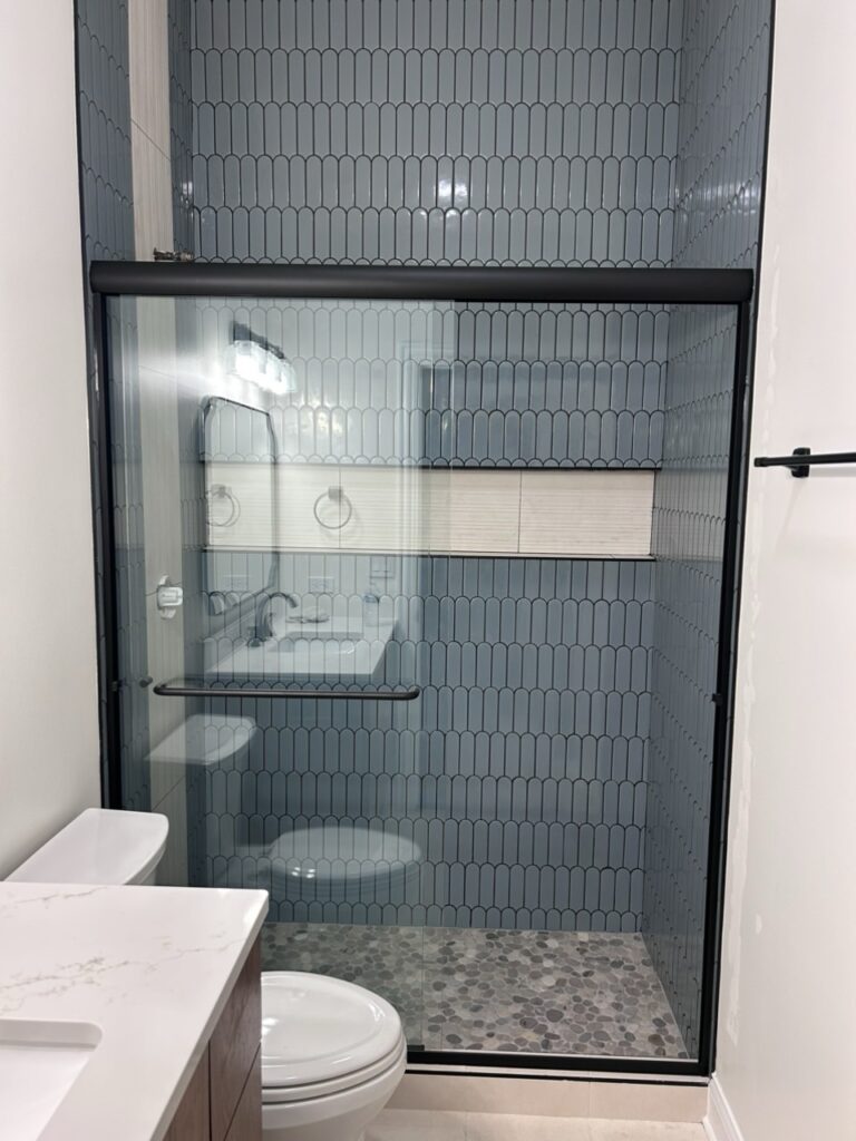 Glass shower enclosure with blue tile walls in a contemporary bathroom setting.